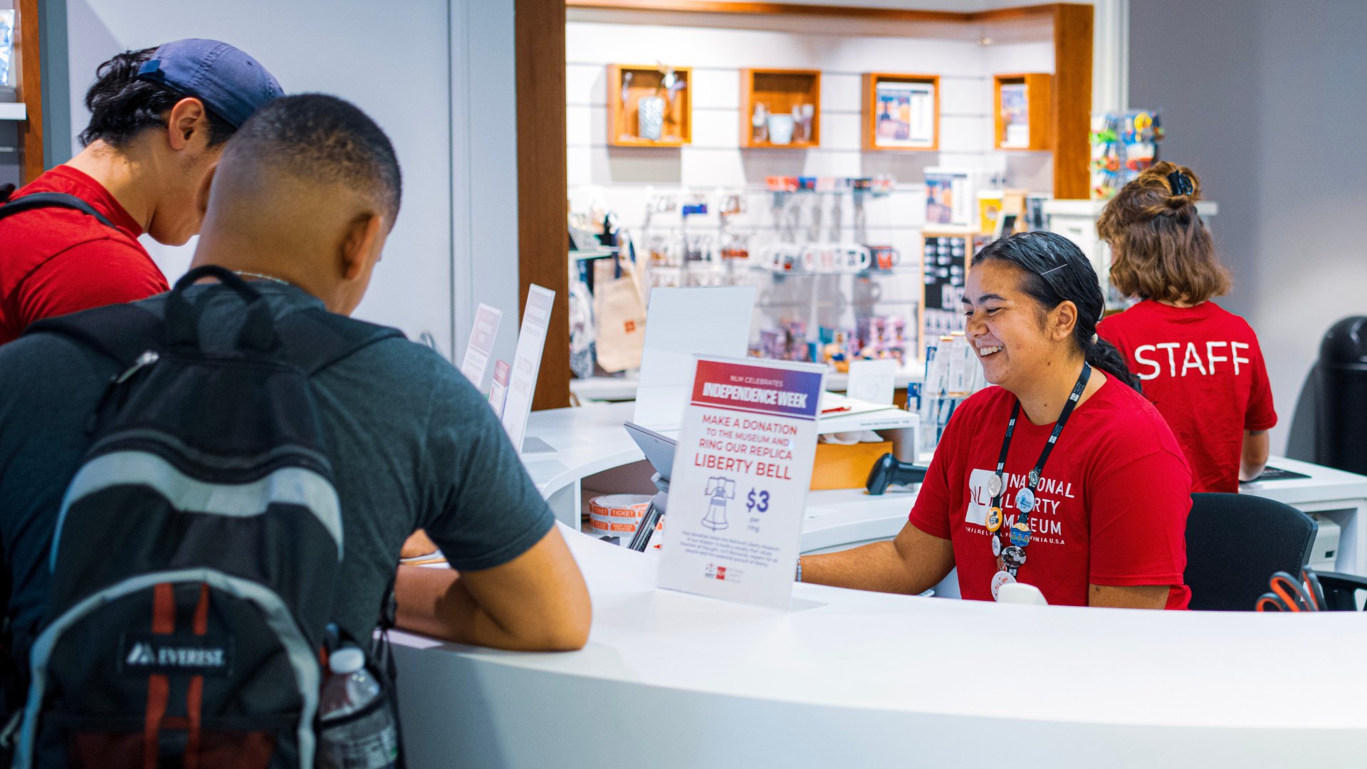 National Liberty Museum Visitor Services staff members engage with two adults at the front desk.